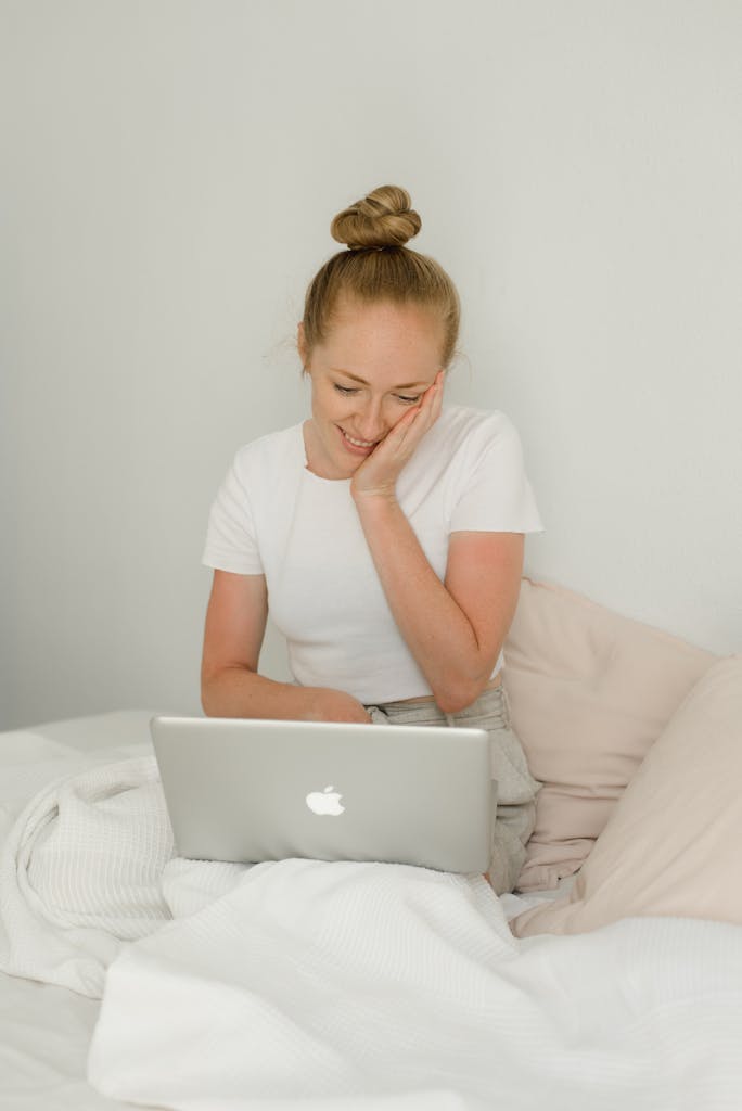 Smiling Woman Sitting with Laptop on Bed